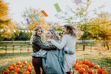three teenage girls dance and laugh among mountain of pumpkins at the fall fair