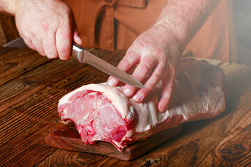 The hunter cuts the meat with a knife on a wooden table. detail on the original piece of meat from...
