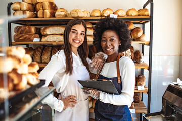 We love our job! Beautiful young women in apron standing in bakery shop. Shot of two women holding...