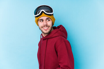 Young caucasian man wearing a ski clothes isolated looks aside smiling, cheerful and pleasant.