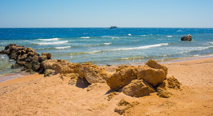 Fototapeta na wymiar sea ​​waves, stones and palm trees on the beach in Sahl Hasheesh, Hurghada, Egypt