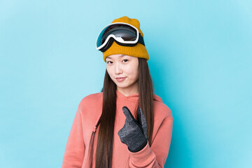 Young chinese woman wearing ski clothes isolated pointing with finger at you as if inviting come closer.