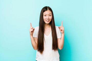Young pretty chinese woman indicates with both fore fingers up showing a blank space.