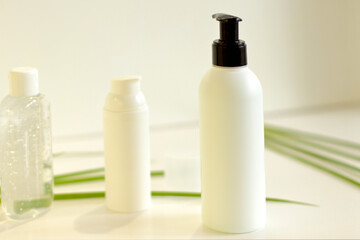 Face/body care concept: bottles of creams/lotions/serums, white plastic jar with green leaves on background