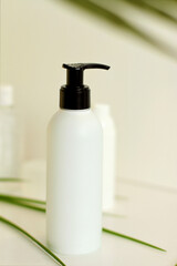 Face/body care concept: bottles of creams/lotions/serums, white plastic jar with green leaves on background