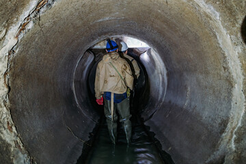 Sewer tunnel worker examines sewer system damage and wastewater leakage