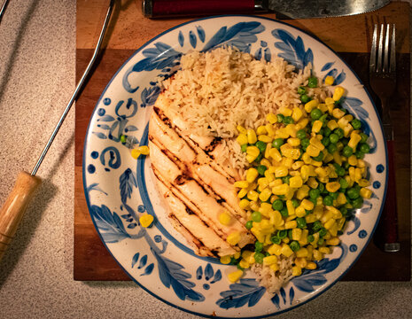 Grilled Chicken Rice Peas and Corn on wood cutting board with grill tool and silverware on counter