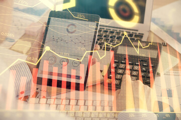 Double exposure of man's hands holding and using a digital device and forex graph drawing. Financial market concept.