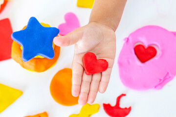 Toddler sculpts from colored plasticine on a white table. The hand of a small child squeezes pieces...