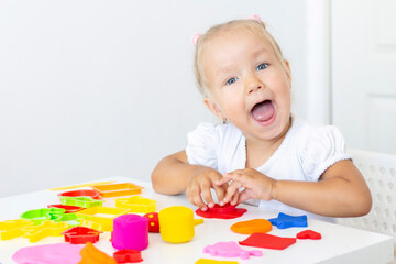 Toddler sculpts from colored plasticine on a white table. The hand of a small child squeezes pieces of colored plasticine. Childrens creativity, educational games, fine motor skills