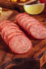 Sliced smoked salami on cutting board with cubs of cheese and olives