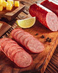 Sliced smoked salami on cutting board with cubs of cheese and olives