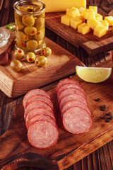 Sliced smoked salami on cutting board with cubs of cheese and olives