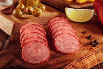 Sliced smoked salami on cutting board with cubs of cheese and olives