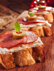 Delicious canapes with salami, cream cheese and olives on a wooden background - Close-up