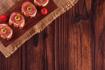 Delicious canapes with salami, cream cheese, olives and tomatos on a wooden background - Top view with copy space