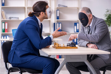 Two businessmen playing chess wearing masks