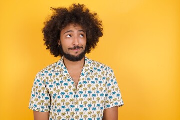 Fototapeta na wymiar Cheerful positive cute handsome nice Young man with afro hair over wearing hawaiian shirt standing over yellow background looking aside into empty space thoughtful