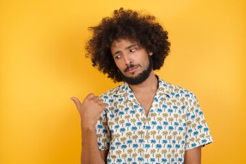 Fototapeta na wymiar charming Young man with afro hair over wearing hawaiian shirt standing over yellow background, promoter looking at copy space having advertisements