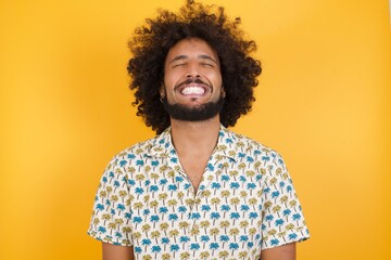 Young man with afro hair over wearing hawaiian shirt standing over yellow background very happy and excited about new plans.