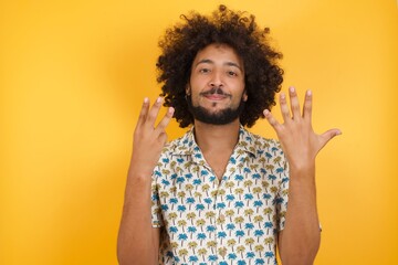 Young man with afro hair over wearing hawaiian shirt standing over yellow background showing and pointing up with fingers number eight while smiling confident and happy.