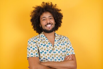 Fototapeta na wymiar Young man with afro hair over wearing hawaiian shirt standing over yellow background happy face smiling with crossed arms looking at the camera. Positive person.