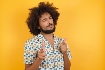 Joyful and charismatic Young man with afro hair over wearing hawaiian shirt standing over yellow...