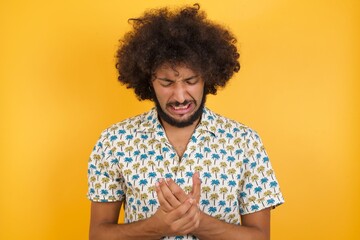 Fototapeta na wymiar Young man with afro hair over wearing hawaiian shirt standing over yellow background Suffering pain on hands and fingers, arthritis inflammation
