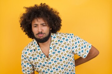 Young man with afro hair over wearing hawaiian shirt standing over yellow background Suffering of backache, touching back with hand, muscular pain