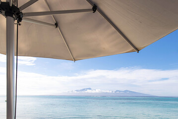 An umbrella provides shade on a tropical island beach with turquoise water