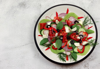 Salad with peppers, cucumbers, olives, onions, and herbs on a round plate on a light gray background. Top view, flat lay
