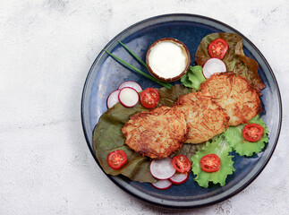 Potato pancakes on a round plate on a light gray background. Top view, flat lay