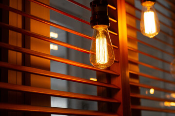 Shining golden antique Edison style bulbs in the restaurant. Lighting decor concept. Vintage light bulb. Blur window jalousie background