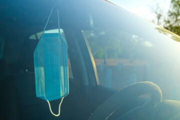 Surgical face mask hanging from the rear view mirror of a car