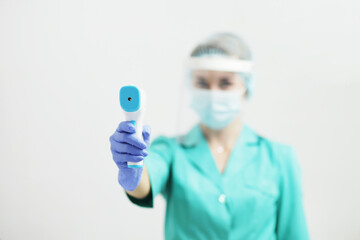 Female doctor or nurse in protective mask at hospital holds pyrometer in hand