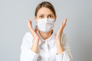 Surprised doctor in mask isolated on gray