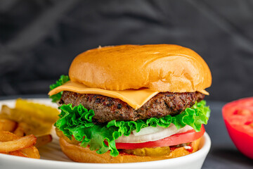 Delicious juicy and spicy burger with slice of tomato, onion, and cheese. Served with fries and pickles.