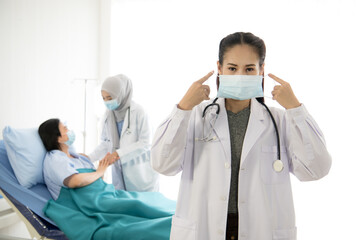 Fototapeta premium Portrait of Asian female doctor wearing protective mask on background of Asian female muslim doctor taking care of patient in hospital room