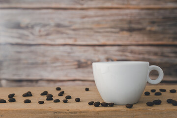 A white hot coffee cup with coffee beans are placed on a wooden plate and on a wooden background.