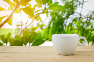 A white hot coffee cup with a spoon in the cup is placed on a wooden plate and on the landscape nature background.