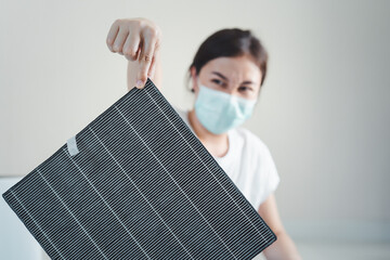Asian woman wearing a hygiene protective face mask during changing a dirty air filter.
