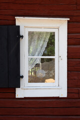 White framed old window on a traditional red Scandinavian cottage. Curtains and oil lamp in the window