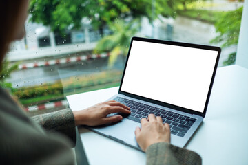 Mockup image of a hand using and typing on laptop computer keyboard with blank white desktop screen in office