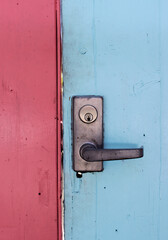 The door handle with a lock at the closed wooden door is pink and blue. Colored wooden entrance doors. Closed door.