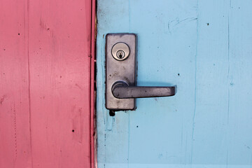 The door handle with a lock at the closed wooden door is pink and blue. Colored wooden entrance doors. Closed door.