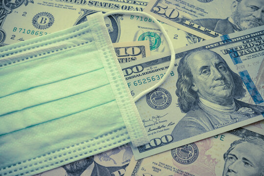 Surgical face mask on US dollar bill banknote background. Concept of global novel coronavirus (Covid-19) outbreak pandemic effect to world economy, financial crisis, investment, stock market, wfh.