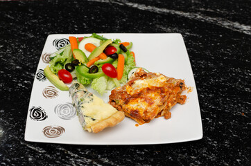 Plato de comida saludable sobre mesa de granito. Ensalada, lasaña, quiche lorraine.