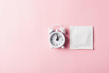 World sexual health or Aids day, condom in wrapper pack and Alarm clock birth control, studio shot isolated on a pink background, Safe sex and reproductive health concept