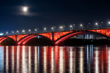 Fototapeta na wymiar Krasnoyarsk, Russia. Night view of Krasnoyarsk Communal bridge with red backlight and Yenisey river.