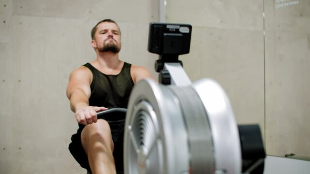 Athlete man training rowing exercise in sport machine in gym club. Fitness man rowing in sport trainer in healthy club
